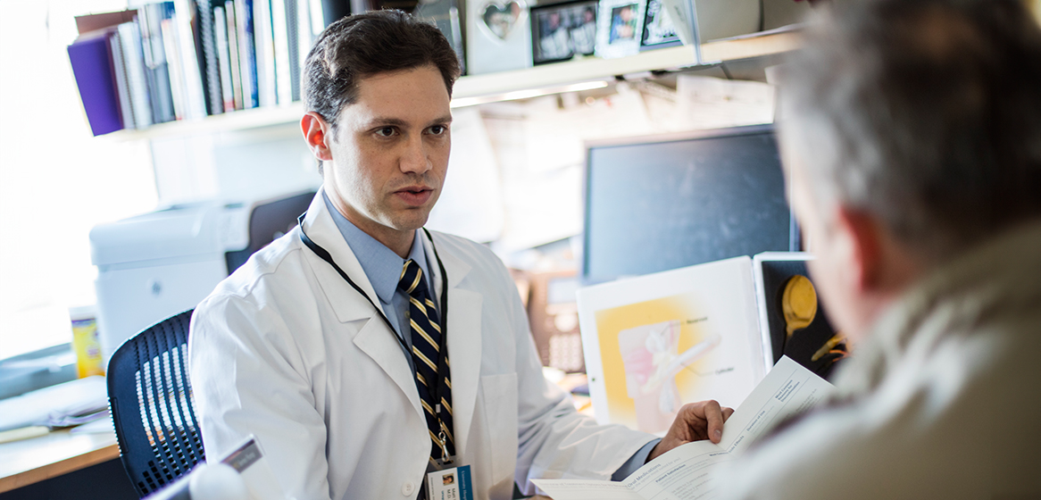 man in white coat at desk talking to older man