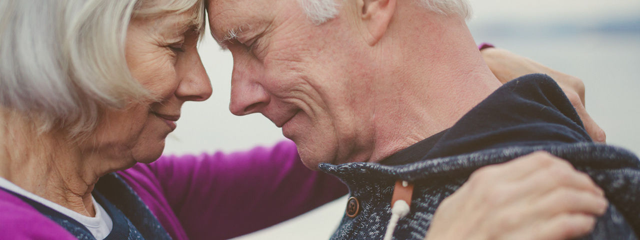 Older woman with arms around an older man looking at each other..