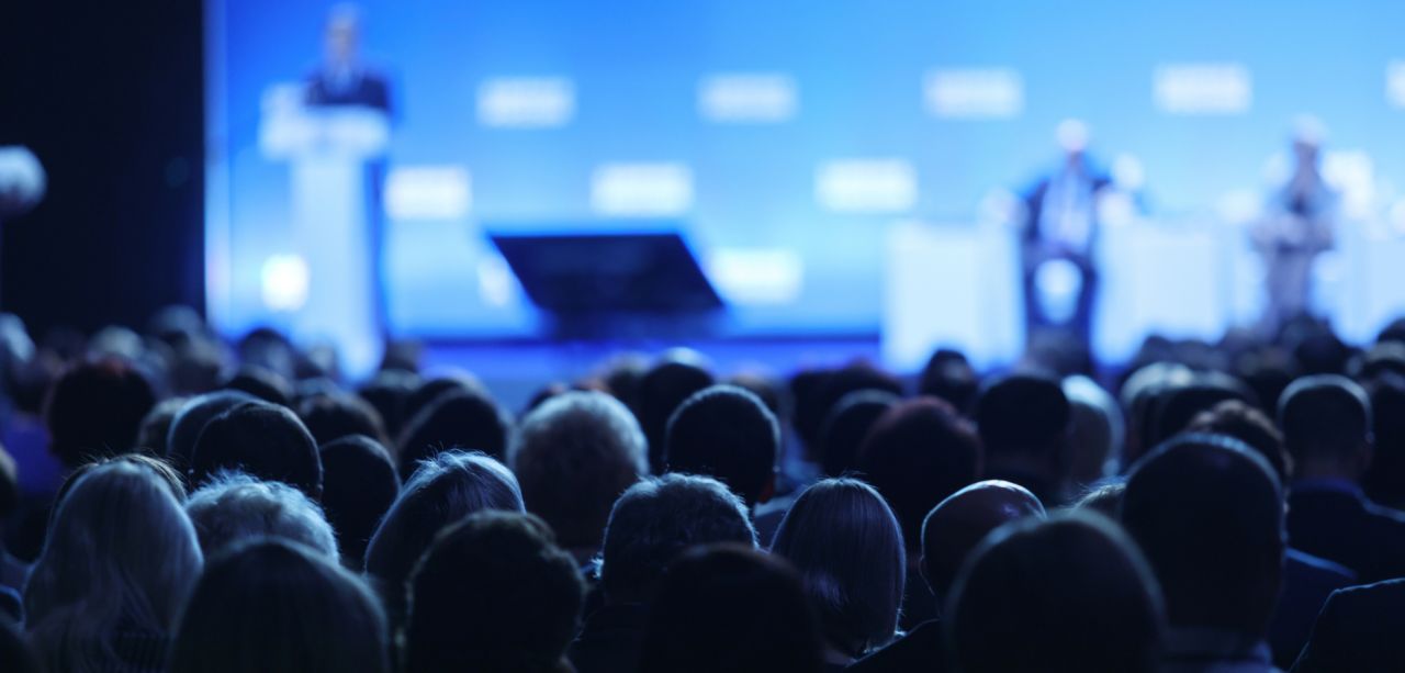 crowd of people in auditorium watching a live seminar.